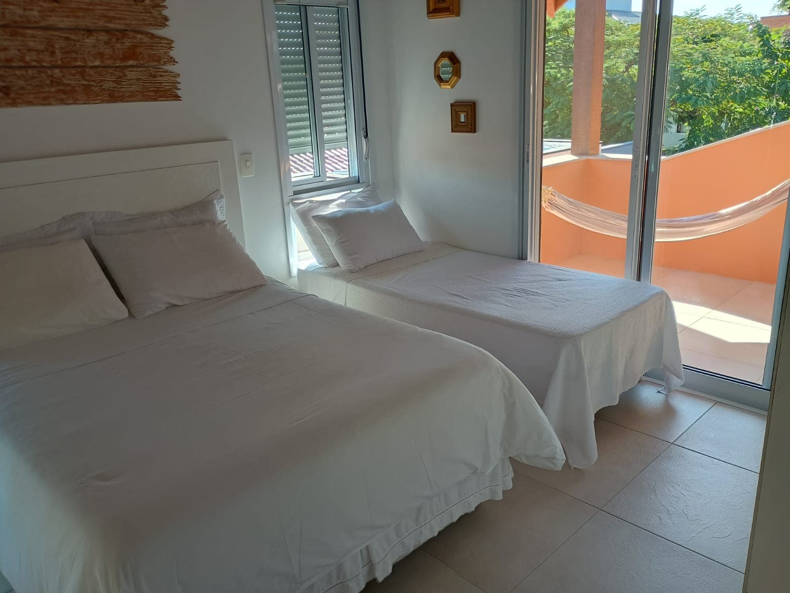 Quarto com cama de casal e cama de solteiro, saída para varanda com rede