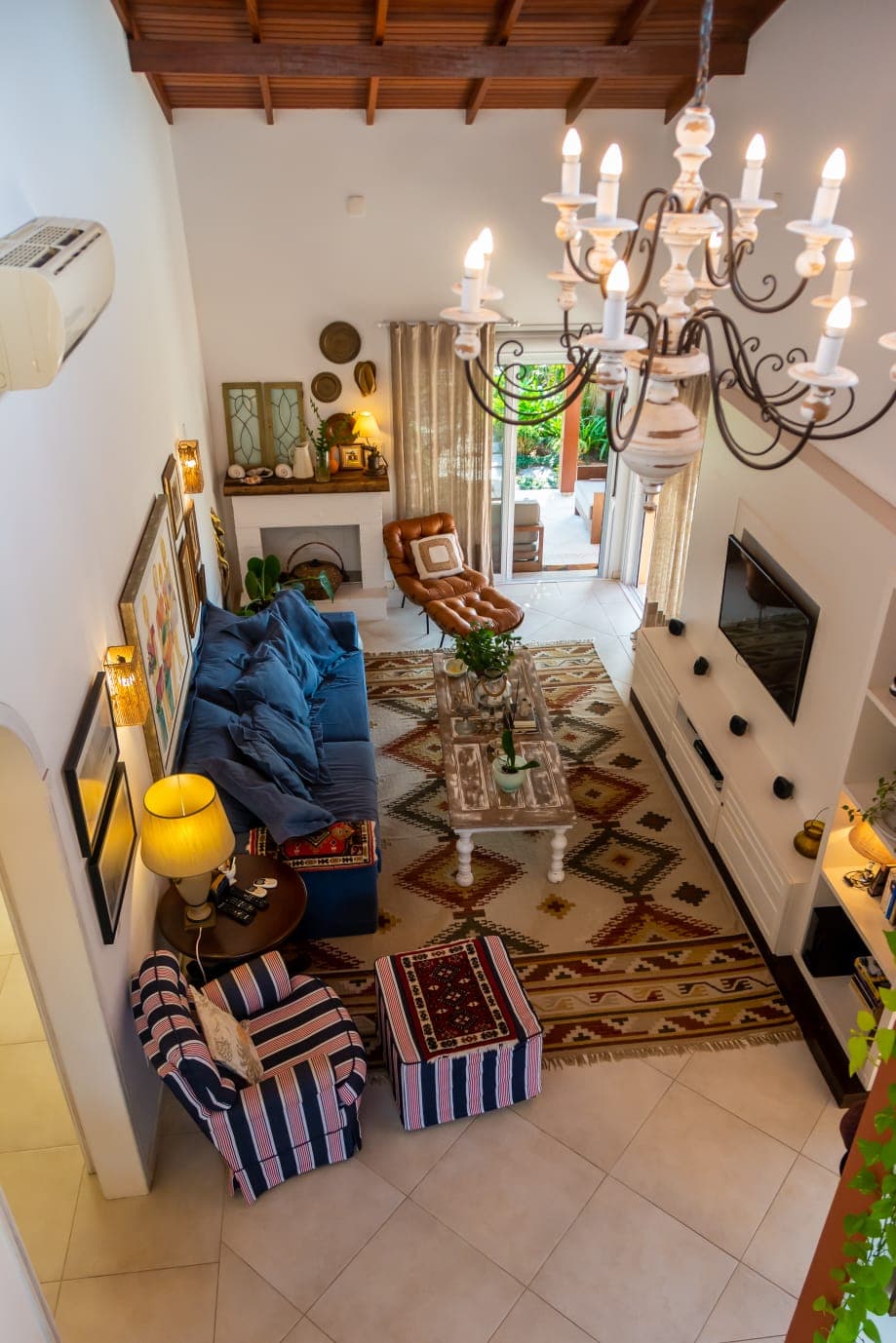 Living em pé-direito duplo com lustre de ferro, sofá azul, tapete kilim e lareira